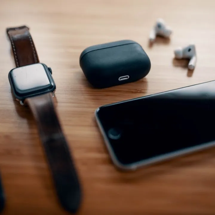 En una mesa se ven dispositivos tecnológicos como celular, audífonos y un reloj inteligente.